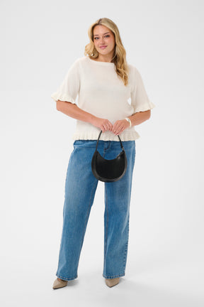 Woman wearing the Kaffe Curve Lindsy Top in White, a white top and blue jeans holding a black handbag on a white background