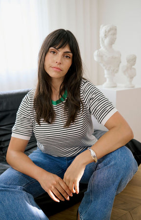 Lady wearing a white top with a black stripe all over and a round green neckline and short sleeves
