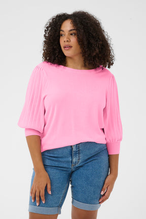 Woman wearing a pink knitted Loni top and blue denim shorts on a white background