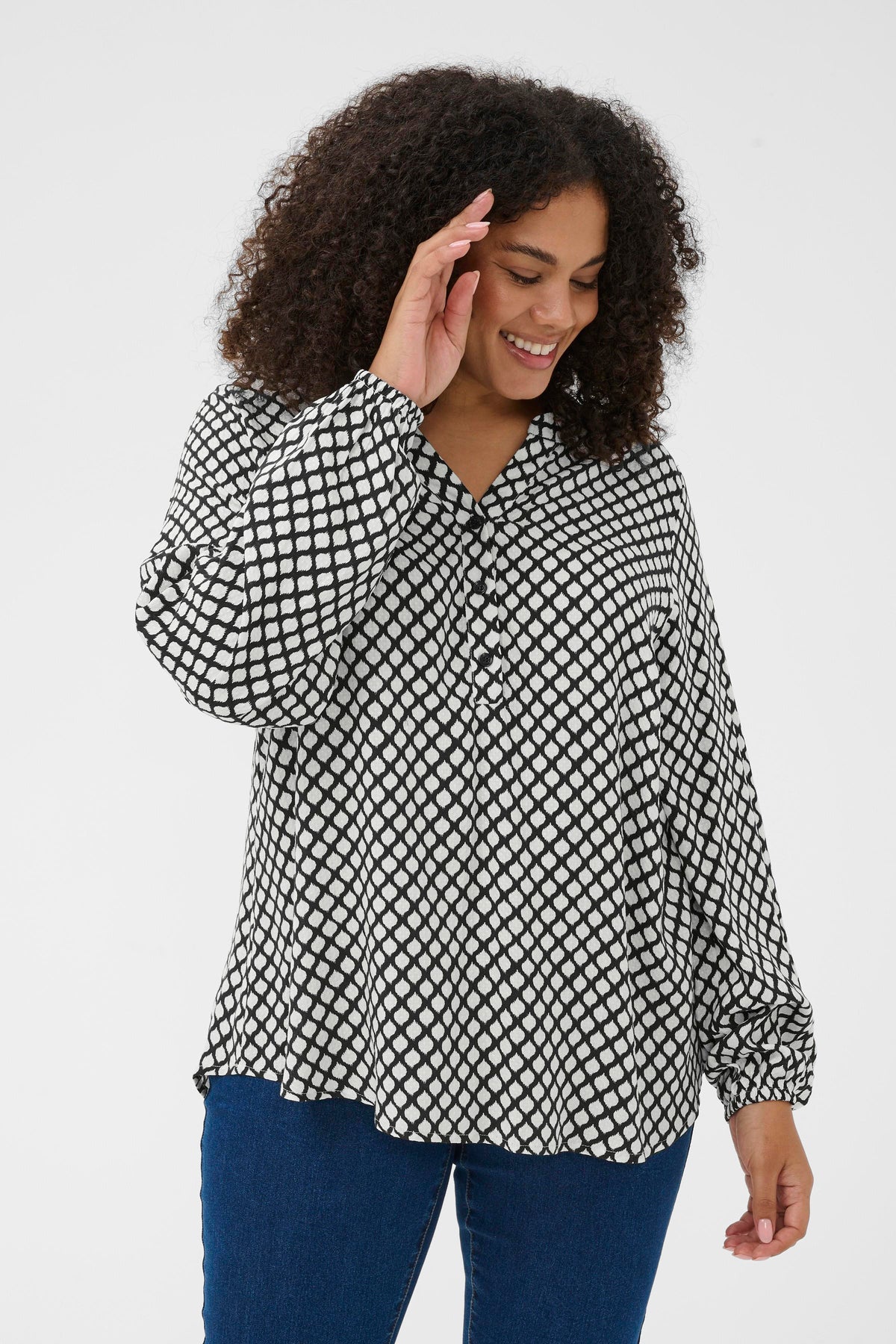 Woman wearing a black and white patterned graphic blouse with blue pants on a white background