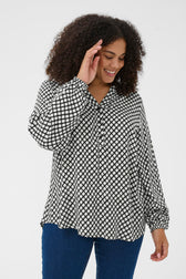 Woman wearing a black and white patterned graphic blouse with blue pants on a white background
