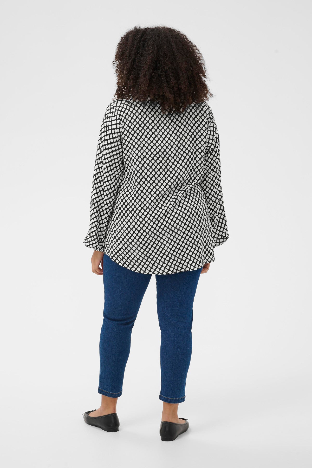 Person wearing a black and white graphic print blouse and jeans on a white background
