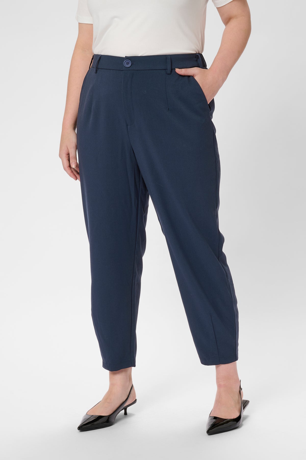 Person wearing navy tapered leg trousers with button closure on a white background