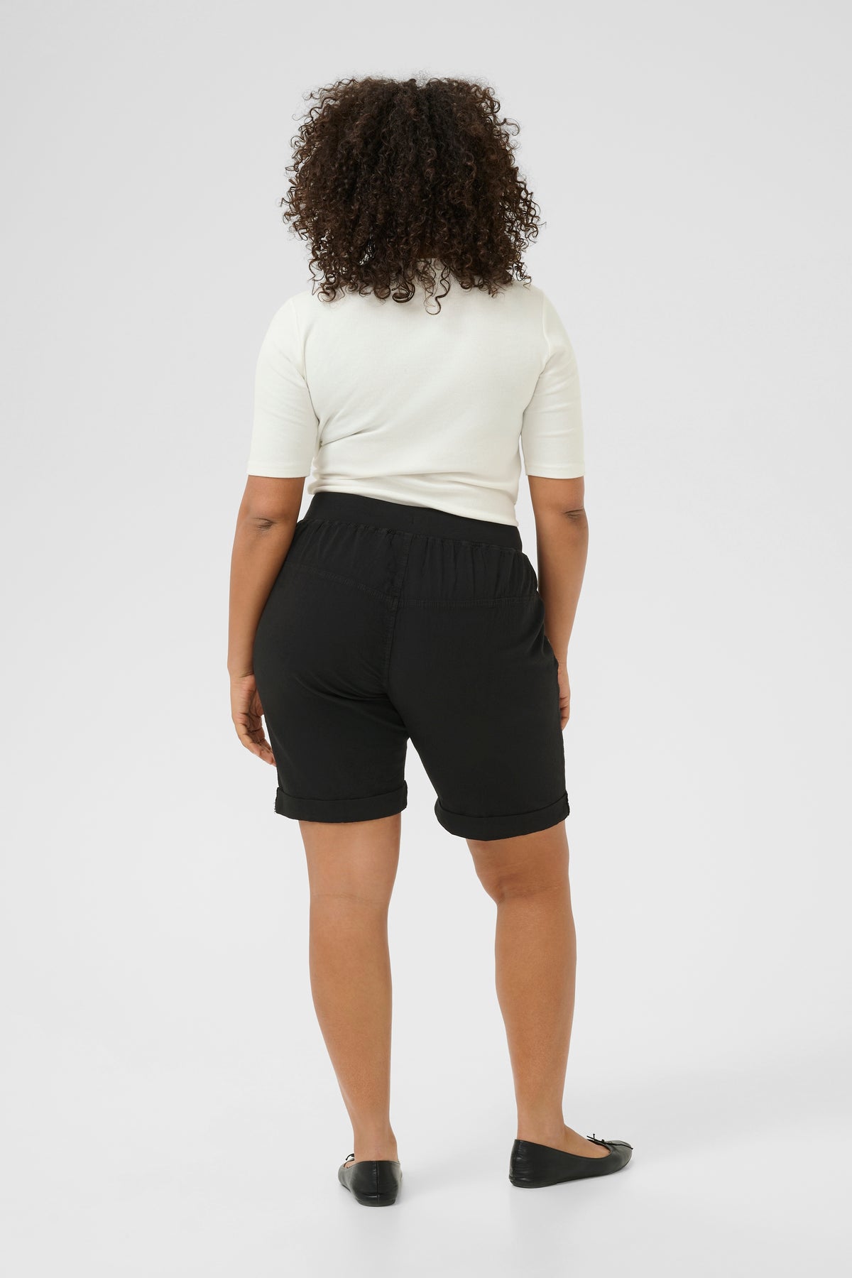 Person wearing black shorts with an elasticated waist band and a white top on a white background