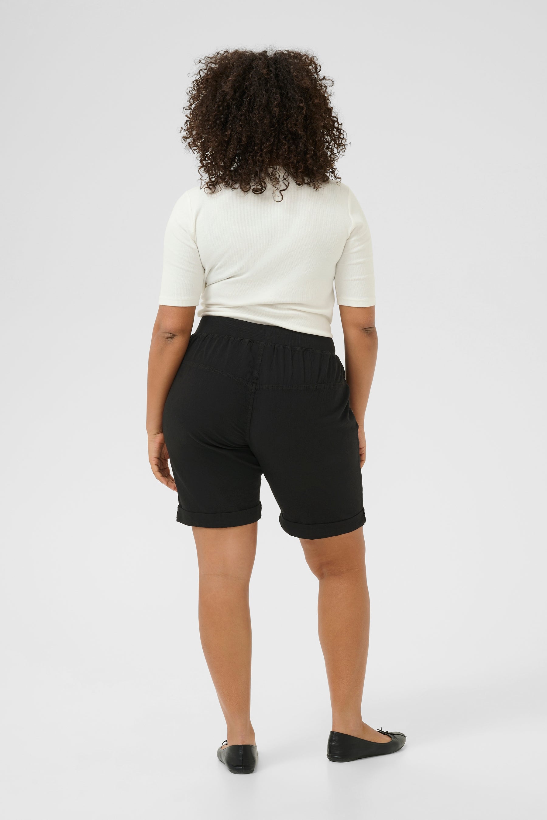 Person wearing black shorts with an elasticated waist band and a white top on a white background