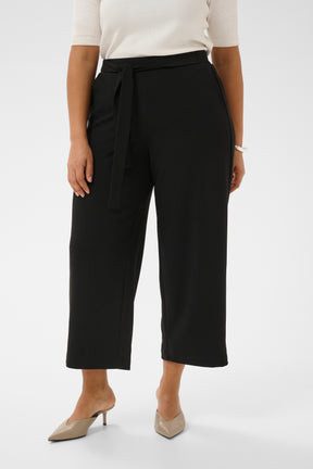 Person wearing black wide leg, ankle grazing trouser that have a built in tie belt with a white top on a white background