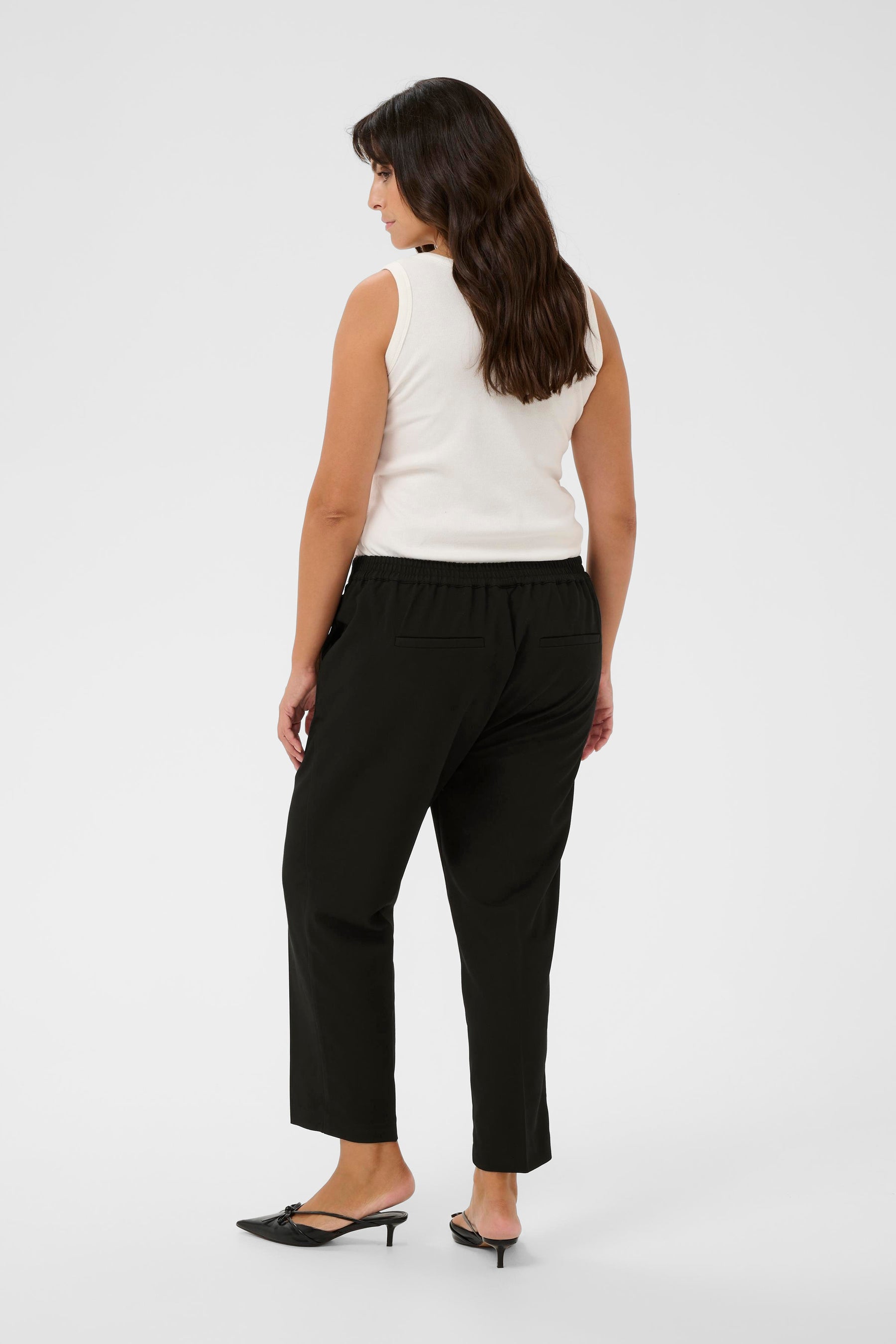 Woman wearing a white sleeveless top and black ankle length trousers on a white background