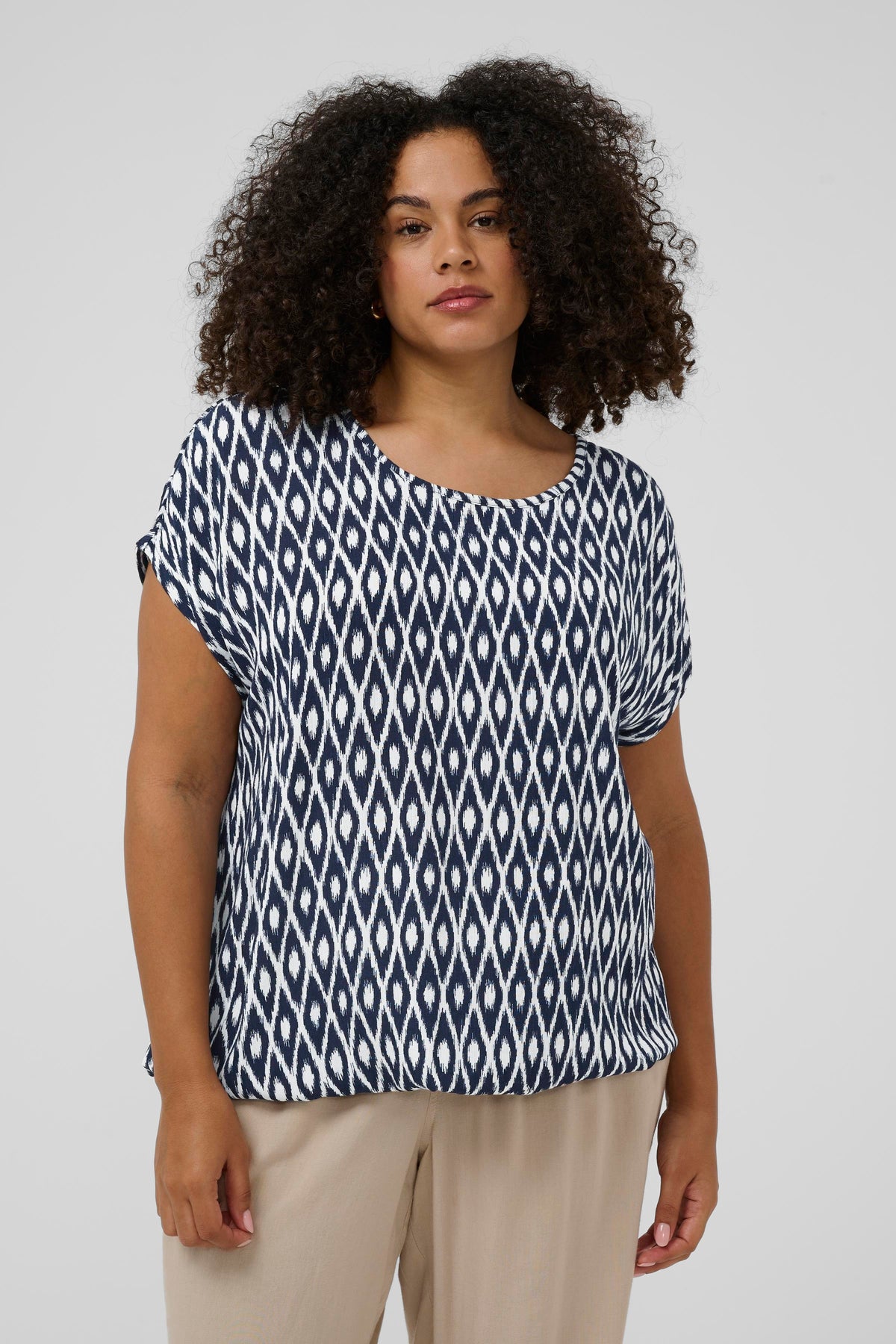 Woman wearing a navy and white patterned top with a round neckline and short sleeves against a plain background