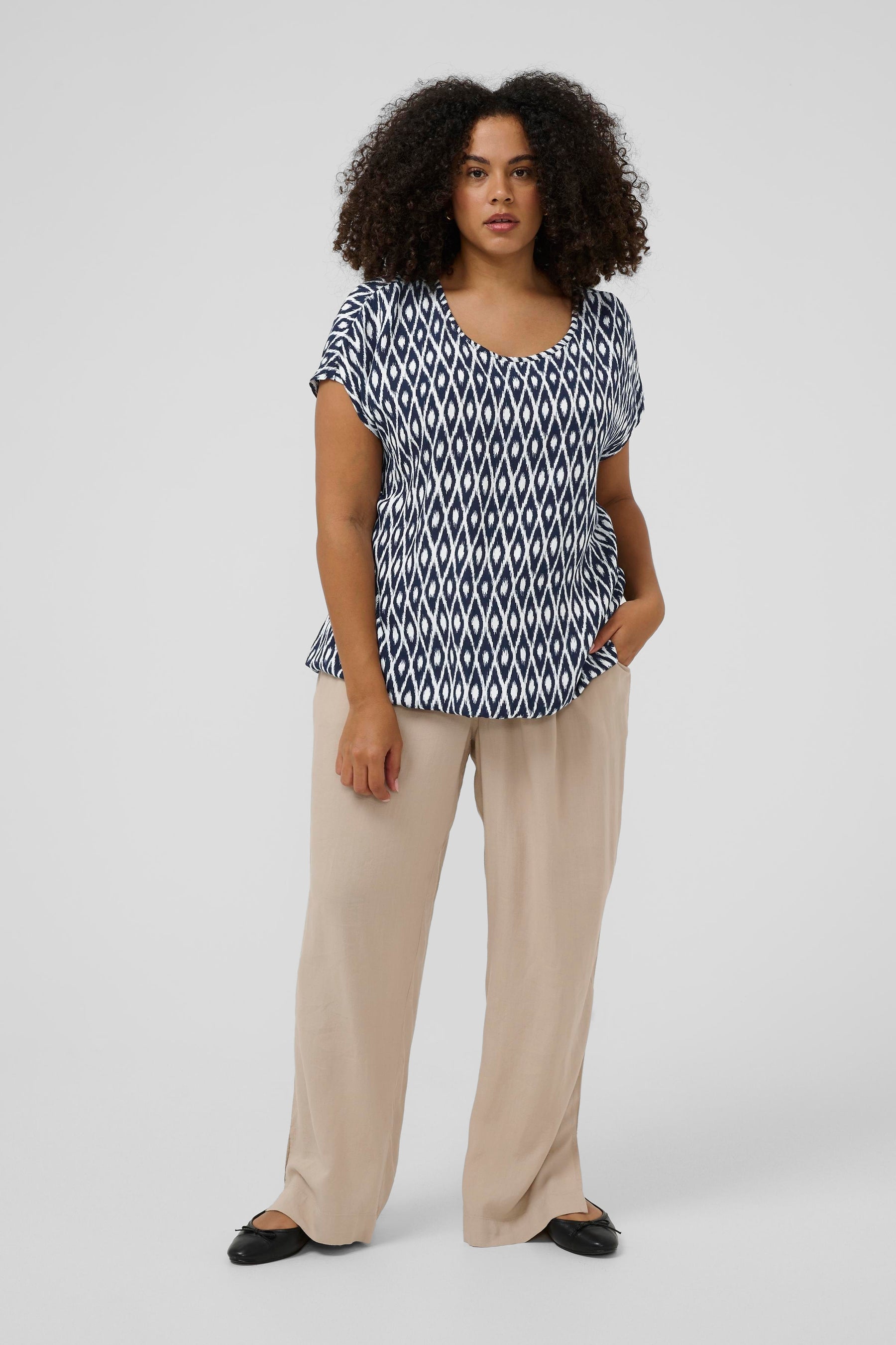 Woman wearing a navy and white top with a round neckline, short sleeves and a loose fit and beige pants on a white background