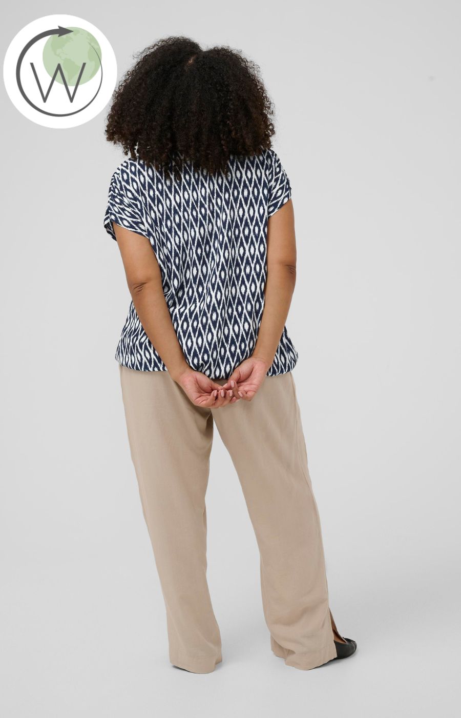 Person wearing a navy and white loose fit top with short sleeves and beige pants on a plain background