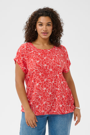 Woman wearing a red floral blouse with a round neckline and short sleeves and blue jeans on a white background