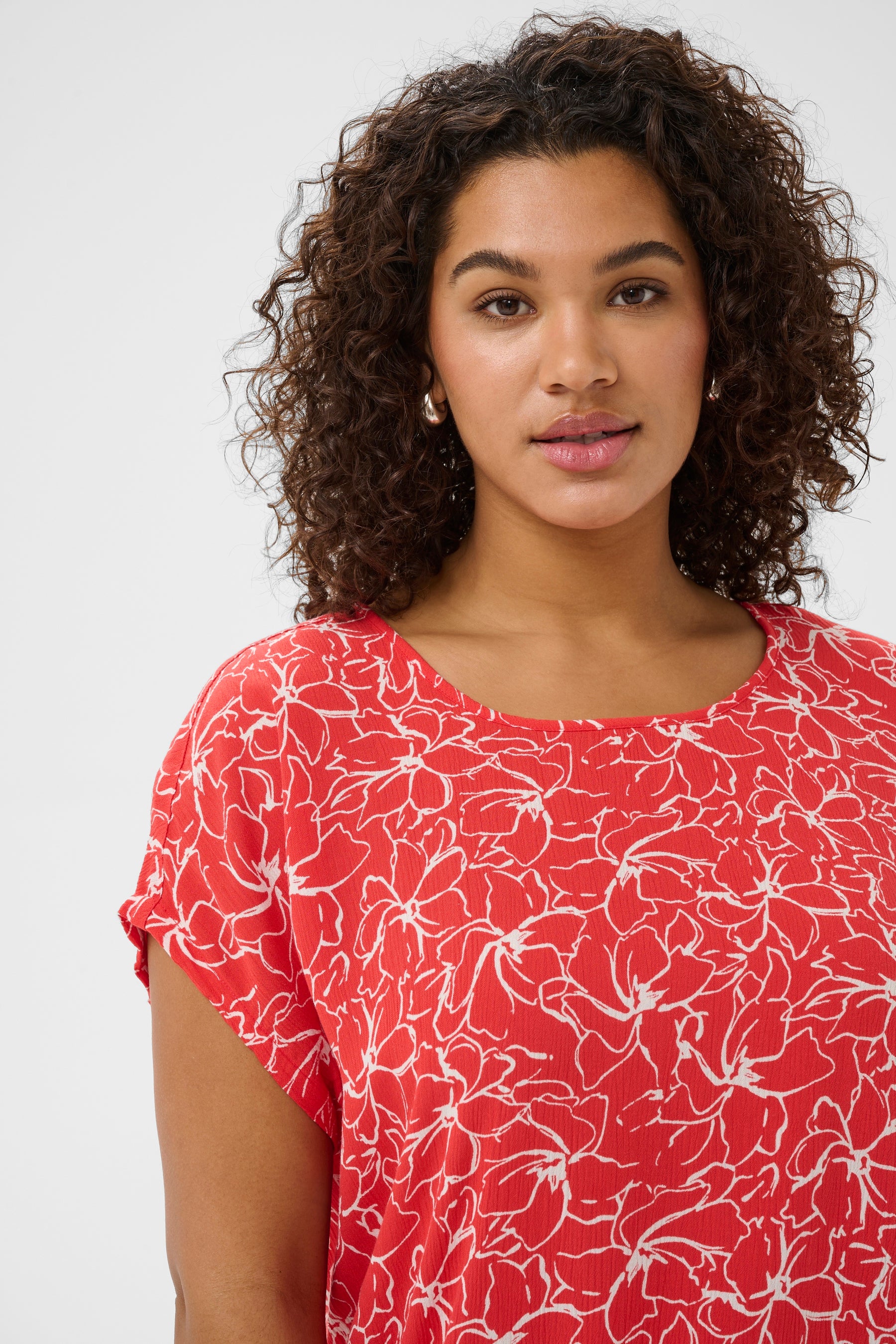 Woman wearing a red floral patterned top with a round neckline and short sleeves against a white background