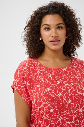 Woman wearing a red floral patterned top with a round neckline and short sleeves against a white background