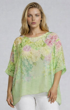 Woman wearing a light green floral blouse with a round neckline and 1/2 length sleeves against a plain background