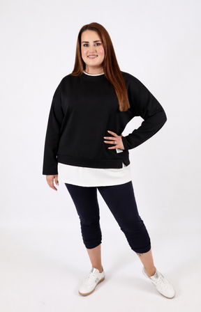 Woman wearing a black sweatshirt with a white trim on a plain background