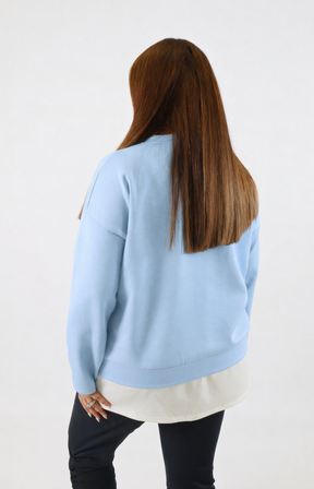 Woman wearing a blue sweatshirt with a white trim on a plain background