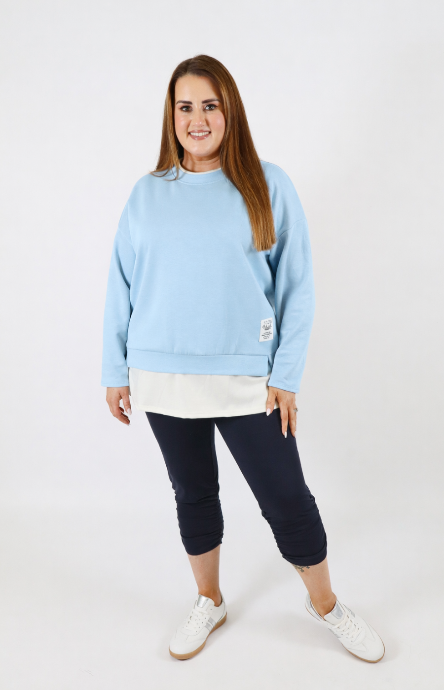 Woman wearing a blue sweatshirt with a white trim on a plain background