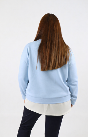Woman wearing a blue sweatshirt with a white trim on a plain background