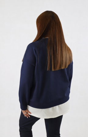 Woman wearing a navy sweatshirt with a white trim on a plain background