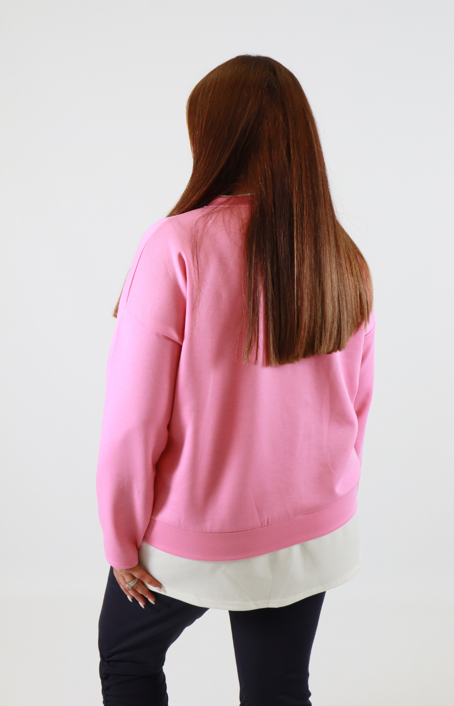 Person wearing a pink sweatshirt with a white shirt underneath on a plain background