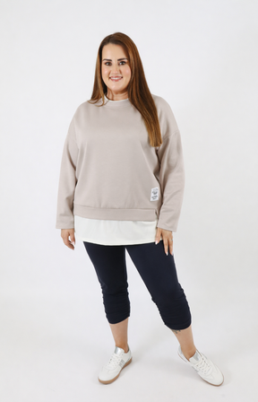 Woman wearing a taupe sweatshirt with a white trim on a plain background