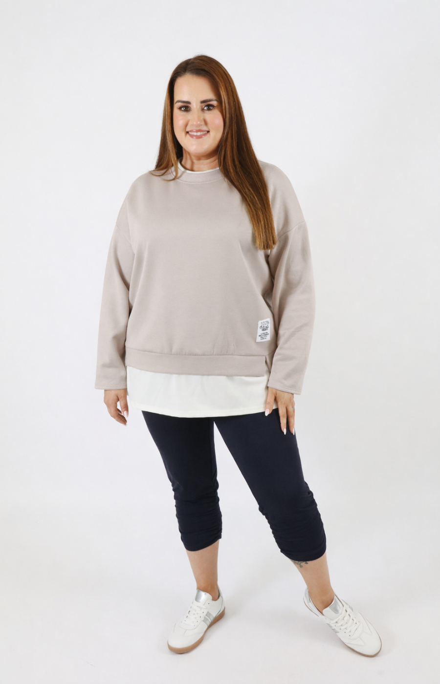 Woman wearing a taupe sweatshirt with a white trim on a plain background