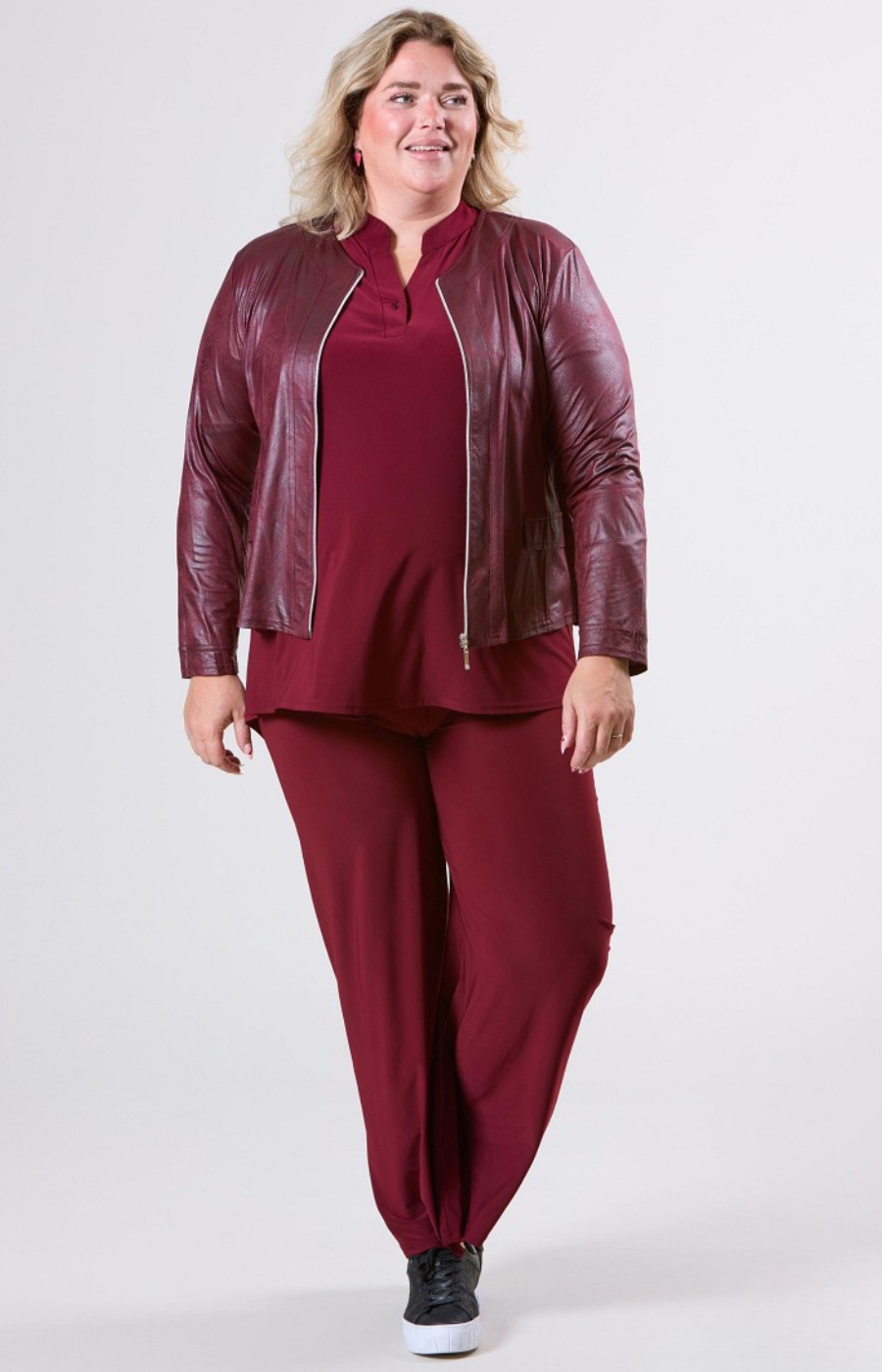 Woman wearing a burgundy leather jacket and matching pants on a white background