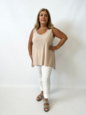 Woman wearing a beige sleeveless top and white pants against a white background