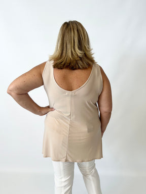Person wearing a beige sleeveless top and white pants on a plain background