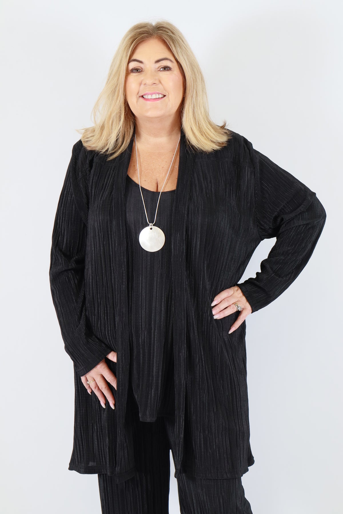 Woman wearing a black plisse cardigan with a white circle pendant on a white background