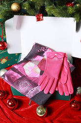 Pink gloves and patterned scarf on a red fabric background with Christmas decorations.