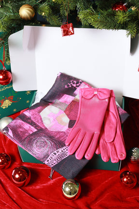 Pink gloves and patterned scarf on a red fabric background with Christmas decorations.