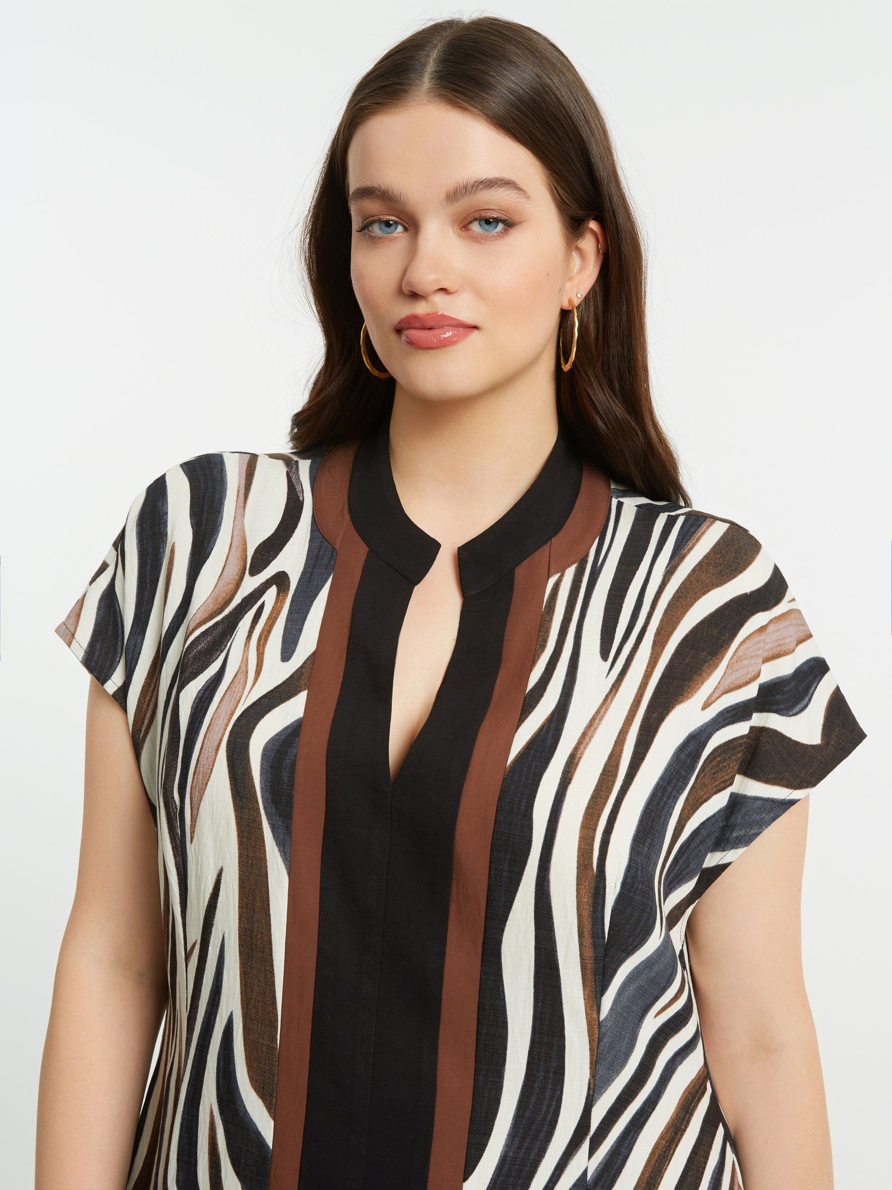 Woman wearing the Mat Animal Print Dress, a zebra print dress with short sleeves and a V neckline with a plain background