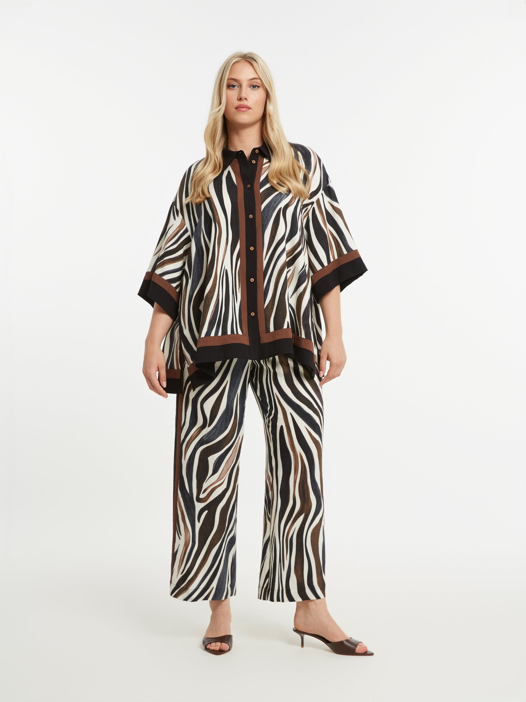 Woman wearing the Mat Animal Print Shirt, an oversized, button up shirt with 1/2 length sleeves and side slits, won with the matching trousers on a white background
