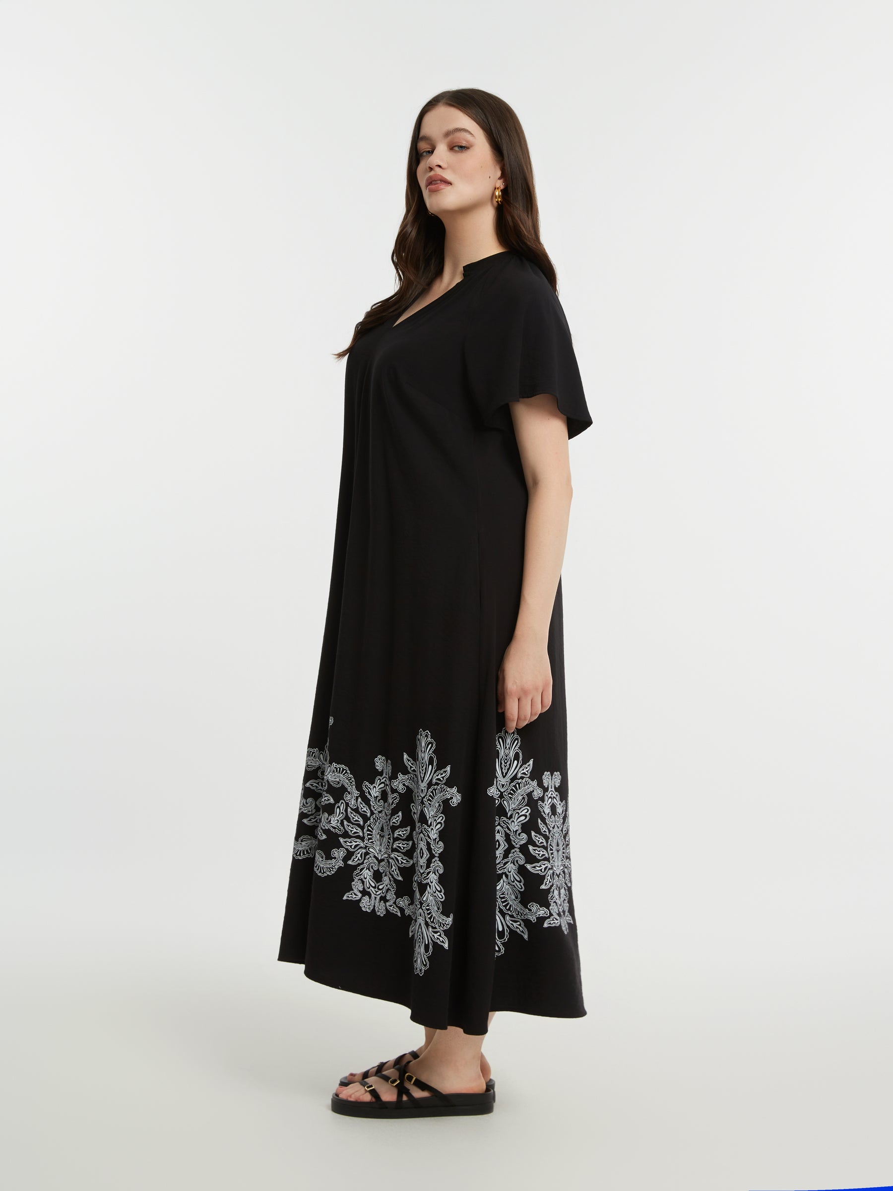 Woman wearing the Mat Black Dress with Paisley Print a black dress with white floral embroidery on a white background
