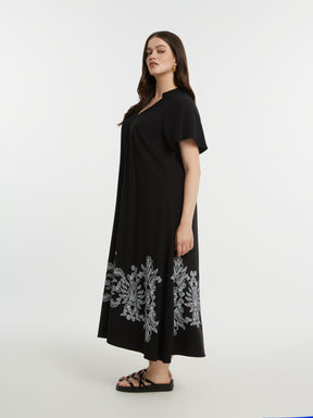 Woman wearing the Mat Black Dress with Paisley Print a black dress with white floral embroidery on a white background