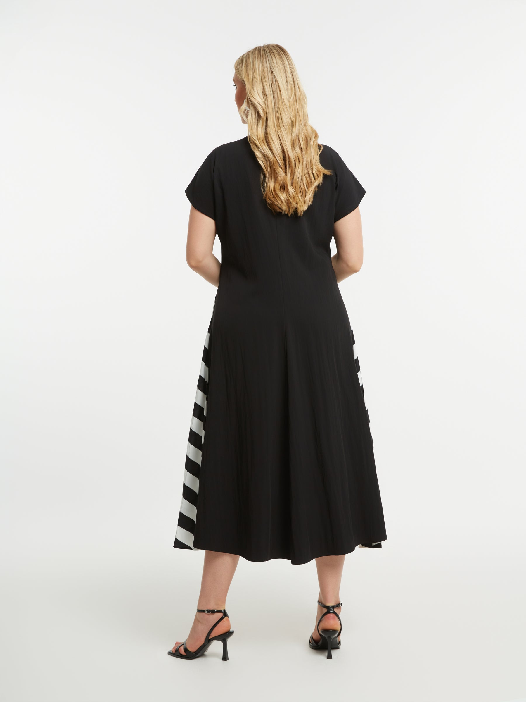 Woman wearing Mat Black Dress with Side Stripes, a black dress with a striped pattern on each side, a midi length, A-line dress with short sleeves on a white background