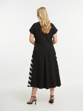 Woman wearing Mat Black Dress with Side Stripes, a black dress with a striped pattern on each side, a midi length, A-line dress with short sleeves on a white background