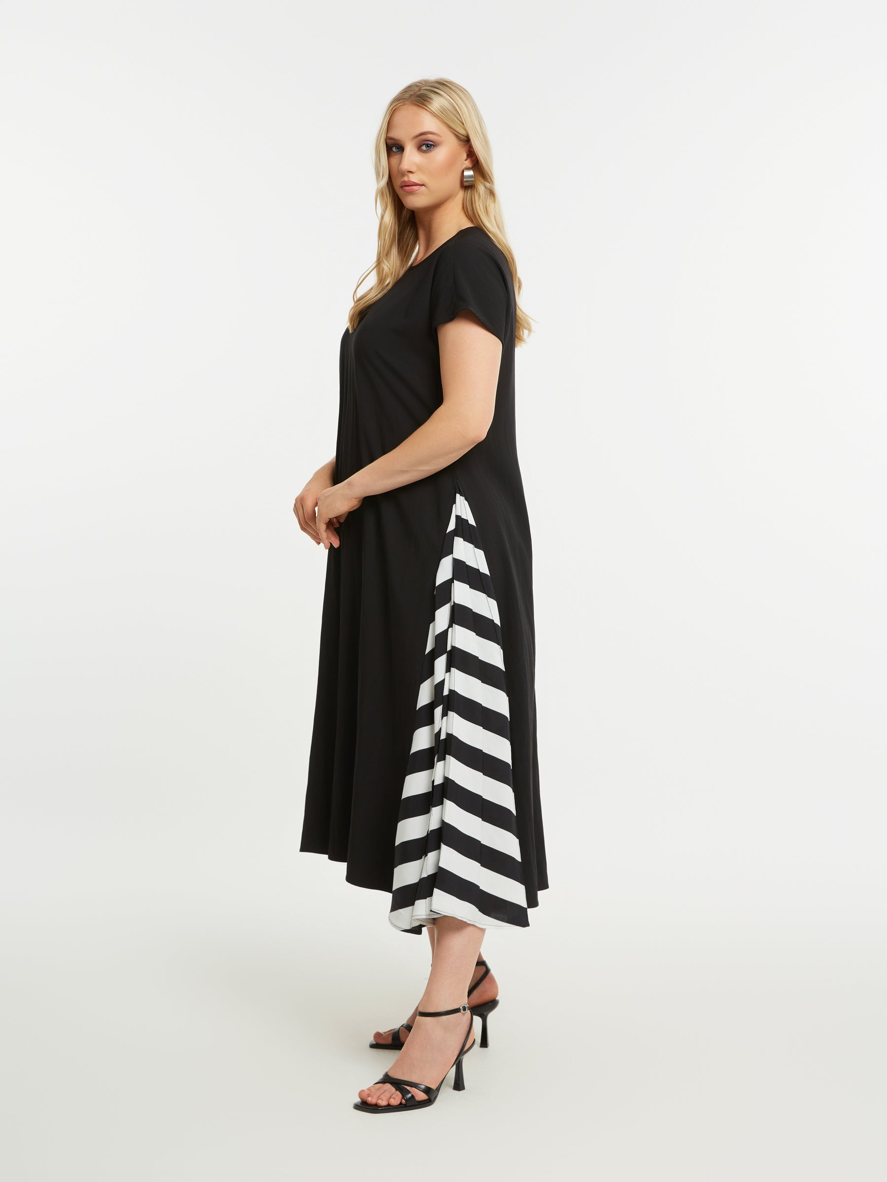 Woman wearing the Mat Black Dress with Side Stripes, a black, A-line midi dress with short sleeves and a round neckline with a white stripe design on each side, on a white background 