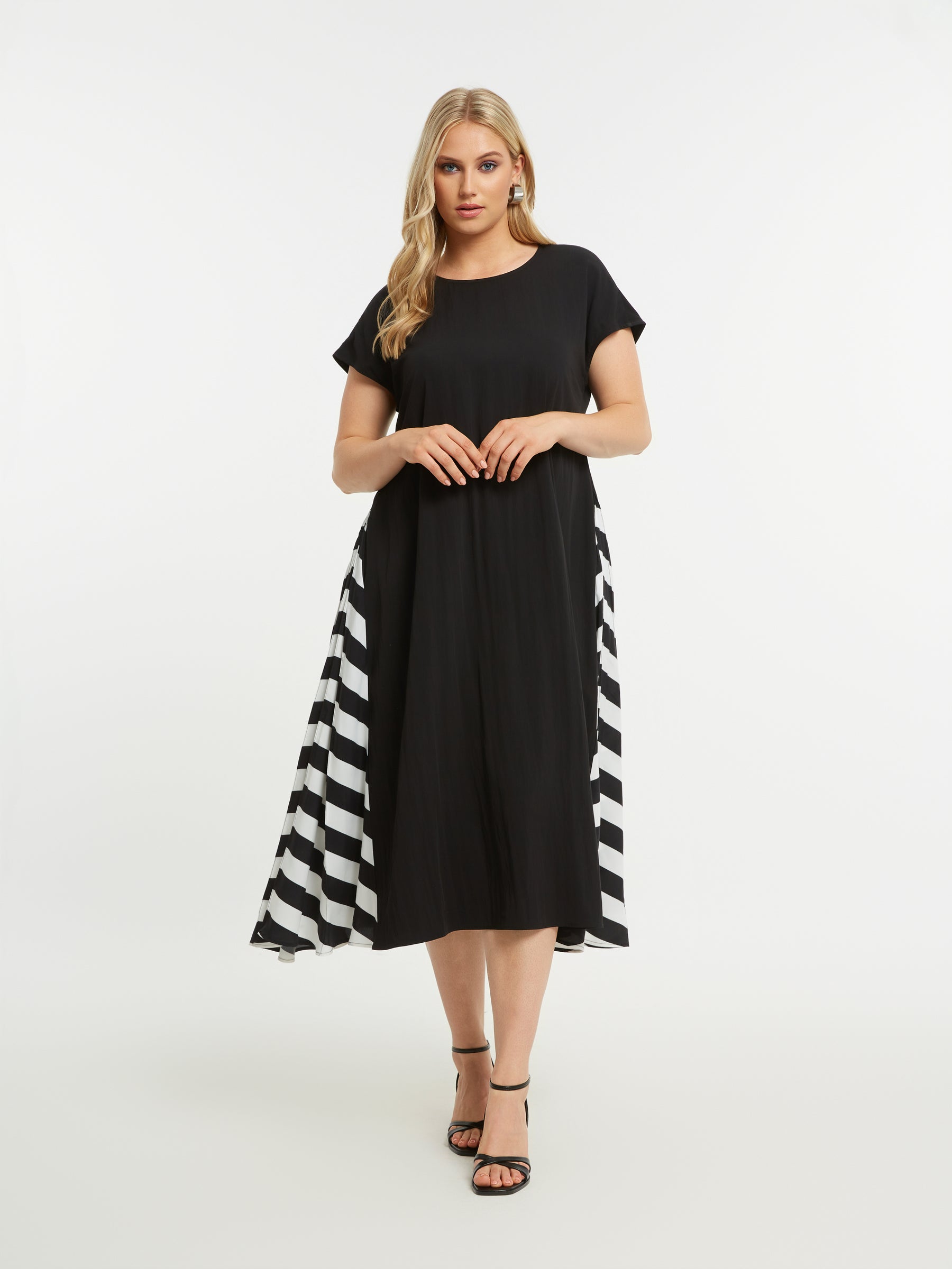 Woman wearing the Mat Black Dress with Side Stripes, a black A-line midi dress with a round neckline and short sleeves and pockets. It also has a striped pattern on a white background