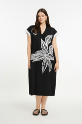 Woman wearing a black dress with a V neckline, short sleeves, midi length and white floral design on a white background