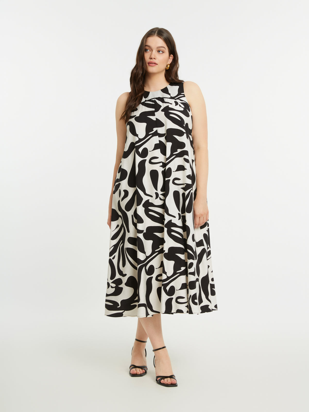 Woman wearing theMat Black and White Swirl Dress, a black and white patterned sleeveless dress with a round neckline, Midi length, and an a-line shape on a white background