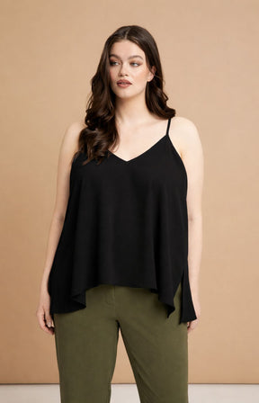 Woman wearing the Mat Cami in Black, a black sleeveless top and green pants against a beige background