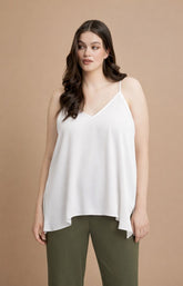 Woman wearing the Mat Cami in White, a white sleeveless top and green pants on a beige background