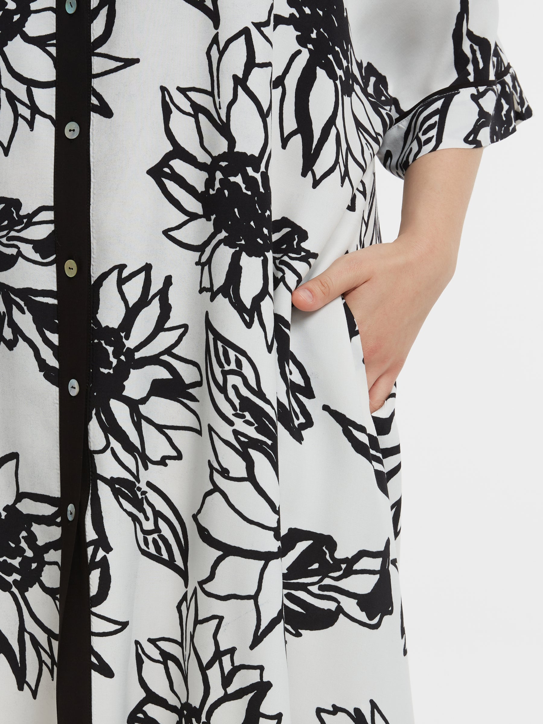 Black floral pattern on a white shirt with a hand in the pocket.
