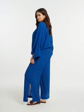 Woman wearing the Mat Slit Trouser in Blue with a blue blouse with a white background