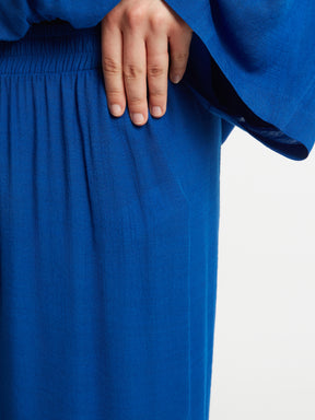 Close-up of a women wearing the Mat Slit Trouser in Blue, showing the elasticated waistband with a plain background