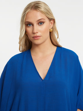 Woman wearing the Mat V Neck Blouse in Blue, a blue blouse with a V neckline and short sleeves on a white background