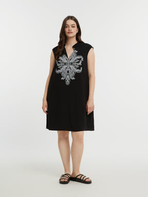 Woman wearing a black sleeveless dress with a V neckline and white embroidery on a white background