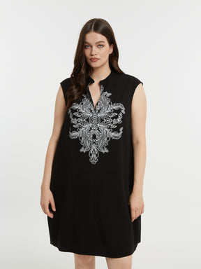 Woman wearing a black sleeveless dress with a V neckline and white embroidery on a white background